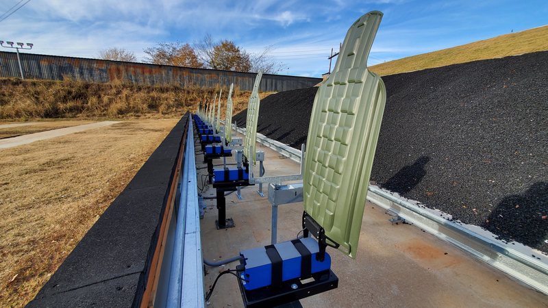 A row of green E-Type silhouettes raised on blue lift units along a rifle range berm.