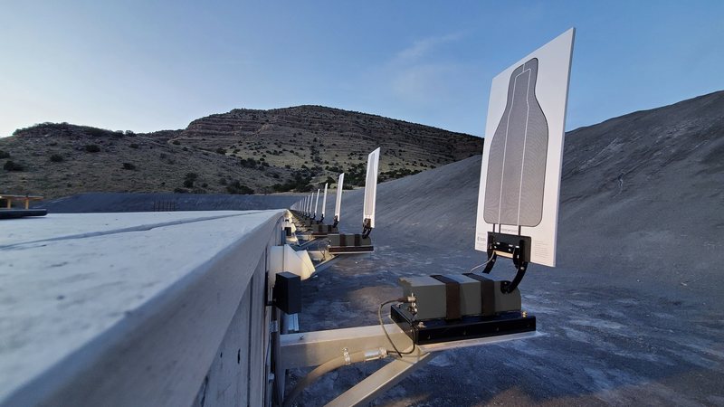 A line of AutoTargets lift units mounted along a concrete berm in desert terrain, each holding a raised paper silhouette target.